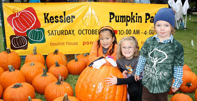 Three children pose outside with a pumpkin in front of a banner that says "Kessler Pumpkin Patch."