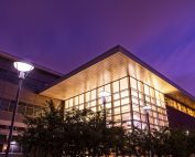 A cubical building at night. The building is mostly glass and light glows within.