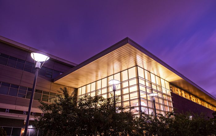 A cubical building at night. The building is mostly glass and light glows within.