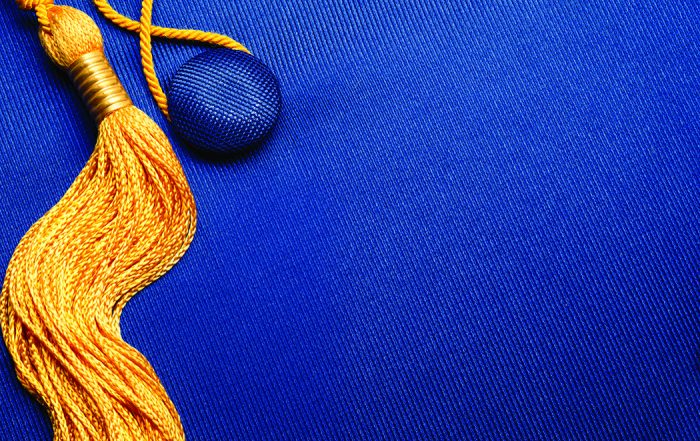 A close up of the top of a graduation cap. It is blue and has a gold tassel.