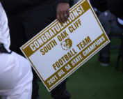 A sign that says 'Congratulations South Oak Cliff Football Team - 2021 UIL 5A State Champions.' In the middle of the sign, there is a logo of a bear.