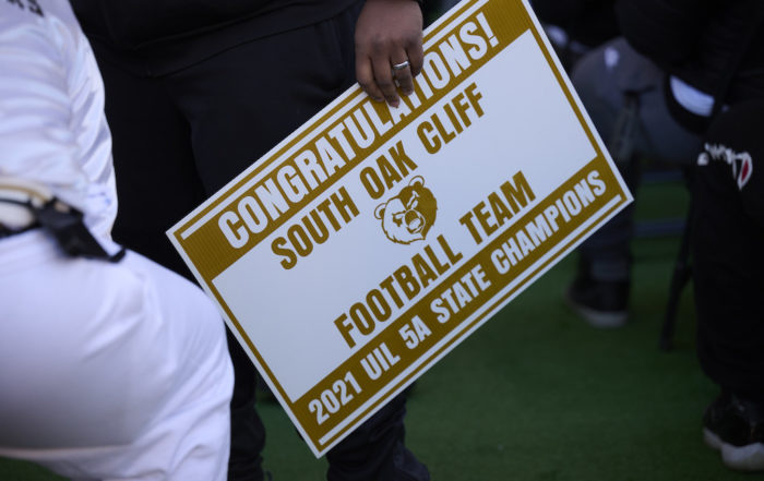A sign that says 'Congratulations South Oak Cliff Football Team - 2021 UIL 5A State Champions.' In the middle of the sign, there is a logo of a bear.
