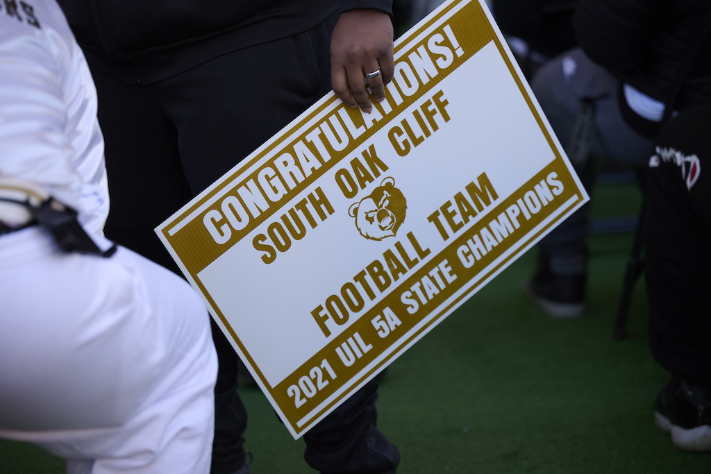 A sign that says 'Congratulations South Oak Cliff Football Team - 2021 UIL 5A State Champions.' In the middle of the sign, there is a logo of a bear.